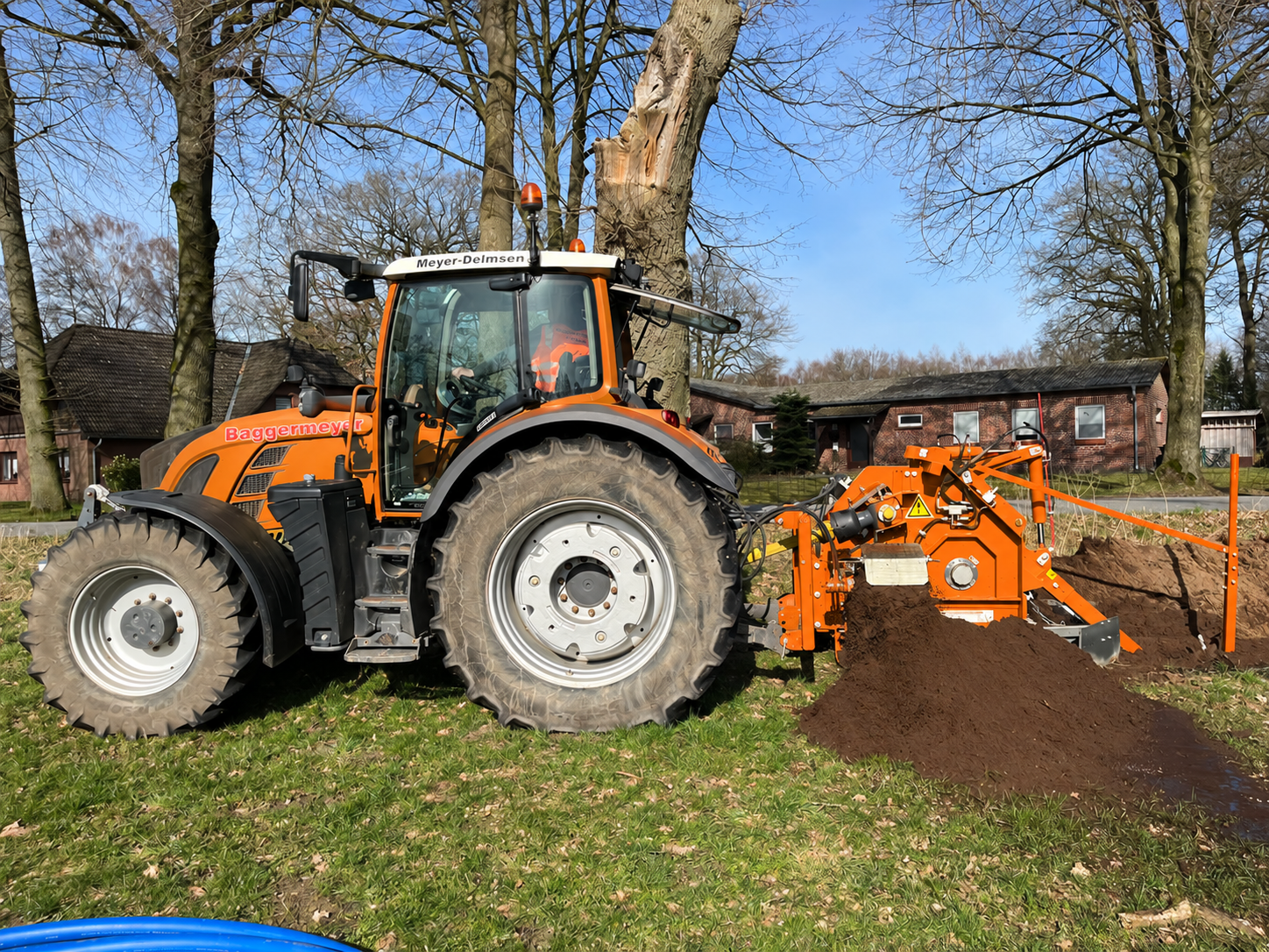 Baggermeyer-Traktor mit orangefarbenem Grabenfräsanbaugerät